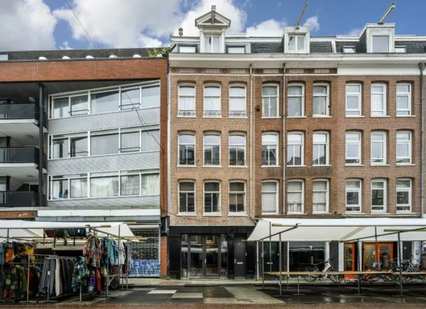 Straatbeeld van de Albert Cuypstraat met marktkramen, fietsen en een mix van moderne en klassieke gevels.